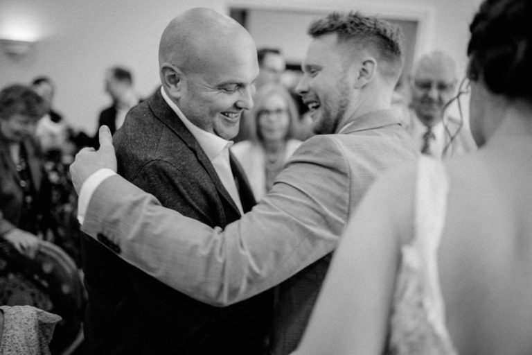 Ein männlicher Gast gratuliert dem Bräutigam und umarmt ihn
