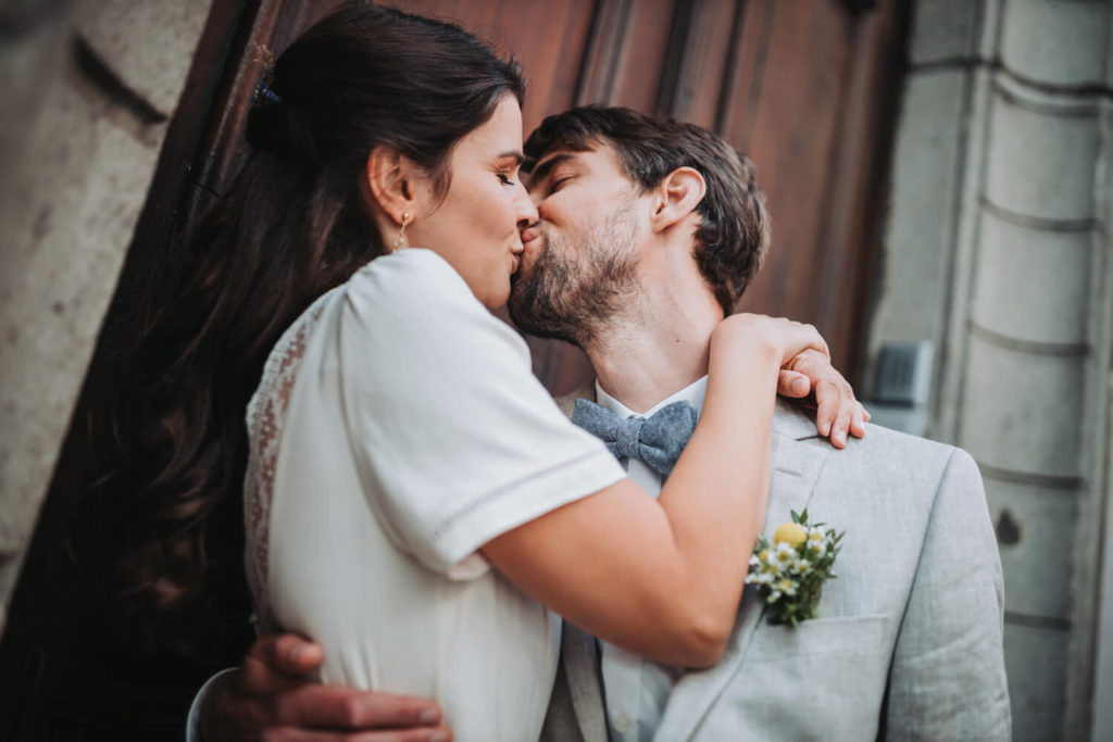 Ein Hochzeitspaar küsst sich innig vor einer braunen, historischen Holztüre