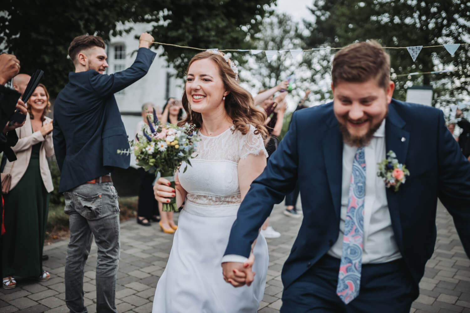Ein Brautpaar läuft Hand in Hand durch ein Spalier und lacht dabei