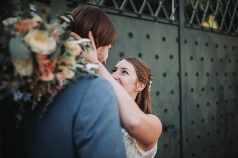 Braut und Bräutigam schauen sich innig in die Augen vor einem grünen Tor, Fotografiert aus dem Rücken des Bräutigams